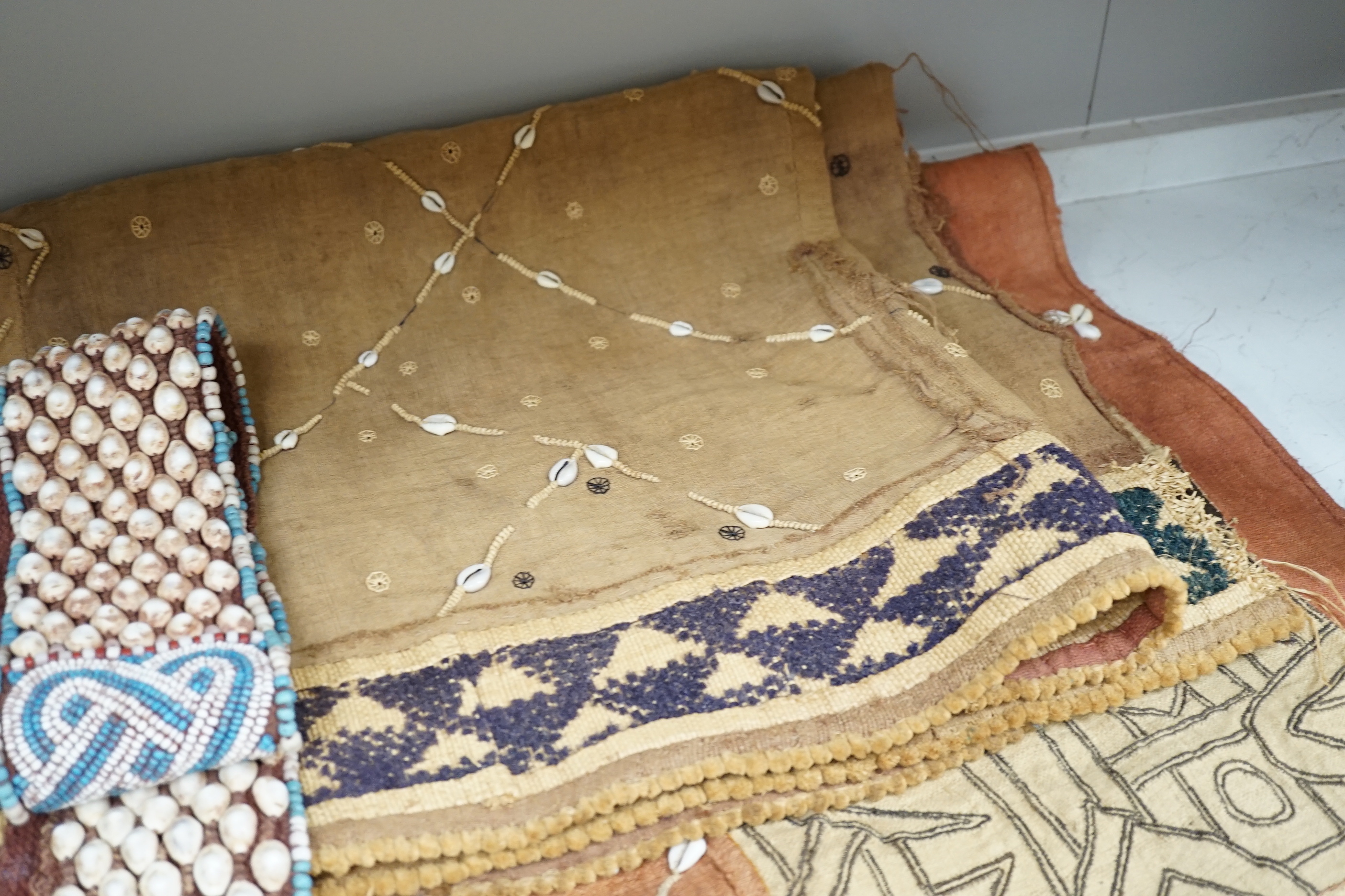 Three African tribal hangings, embroidered with coloured hand dyed threads and appliquéd shells on smaller handwoven cloth panels all sewn together to form the hangings, including a chieftains coloured bead worked and sh